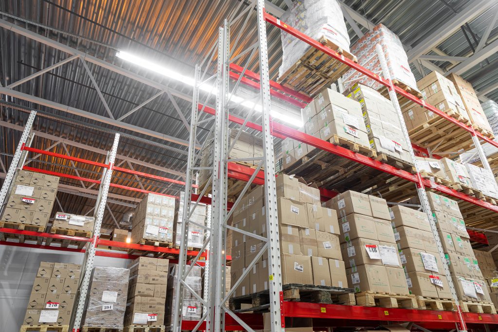 Interior of a logistics centre containing tall red racking stocked with cardboard boxes on pallets.
