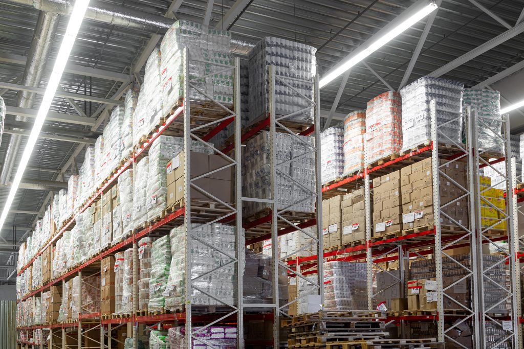 Interior of a large warehouse containing floor to ceiling racking which is packed with goods on pallets.